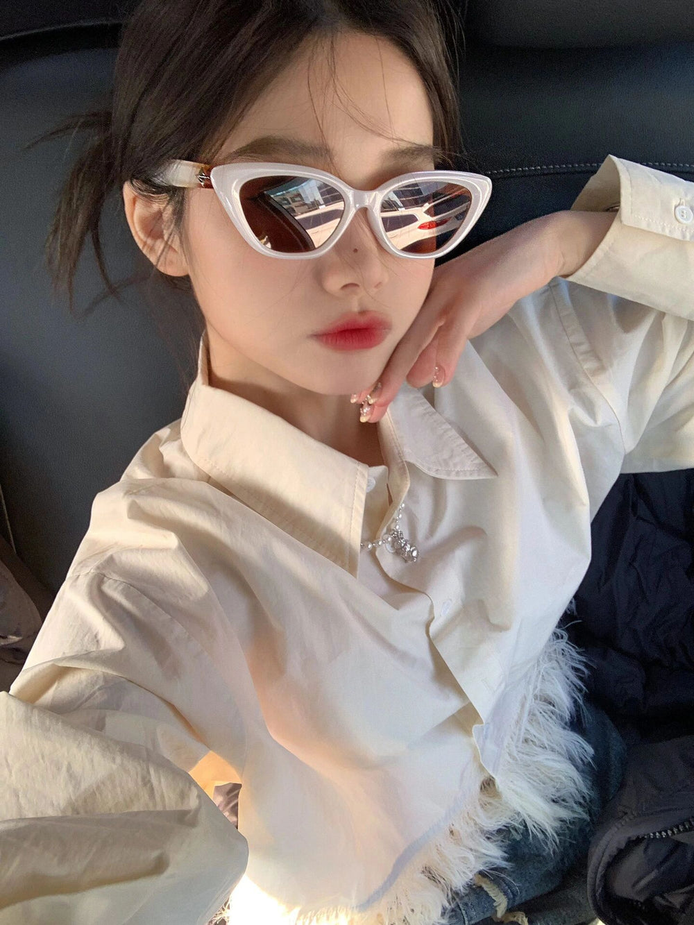 Adorned in a pristine white shirt, the woman exudes an air of refinement, her eyes concealed behind fashionable sunglasses, adding allure to her ensemble.