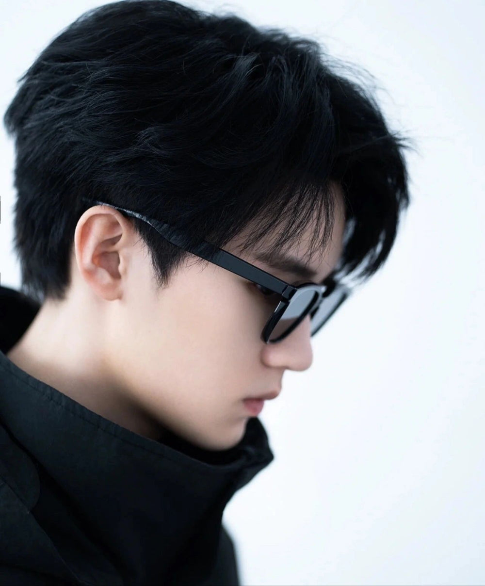 A stylish man with black hair and sunglasses looking downwards.