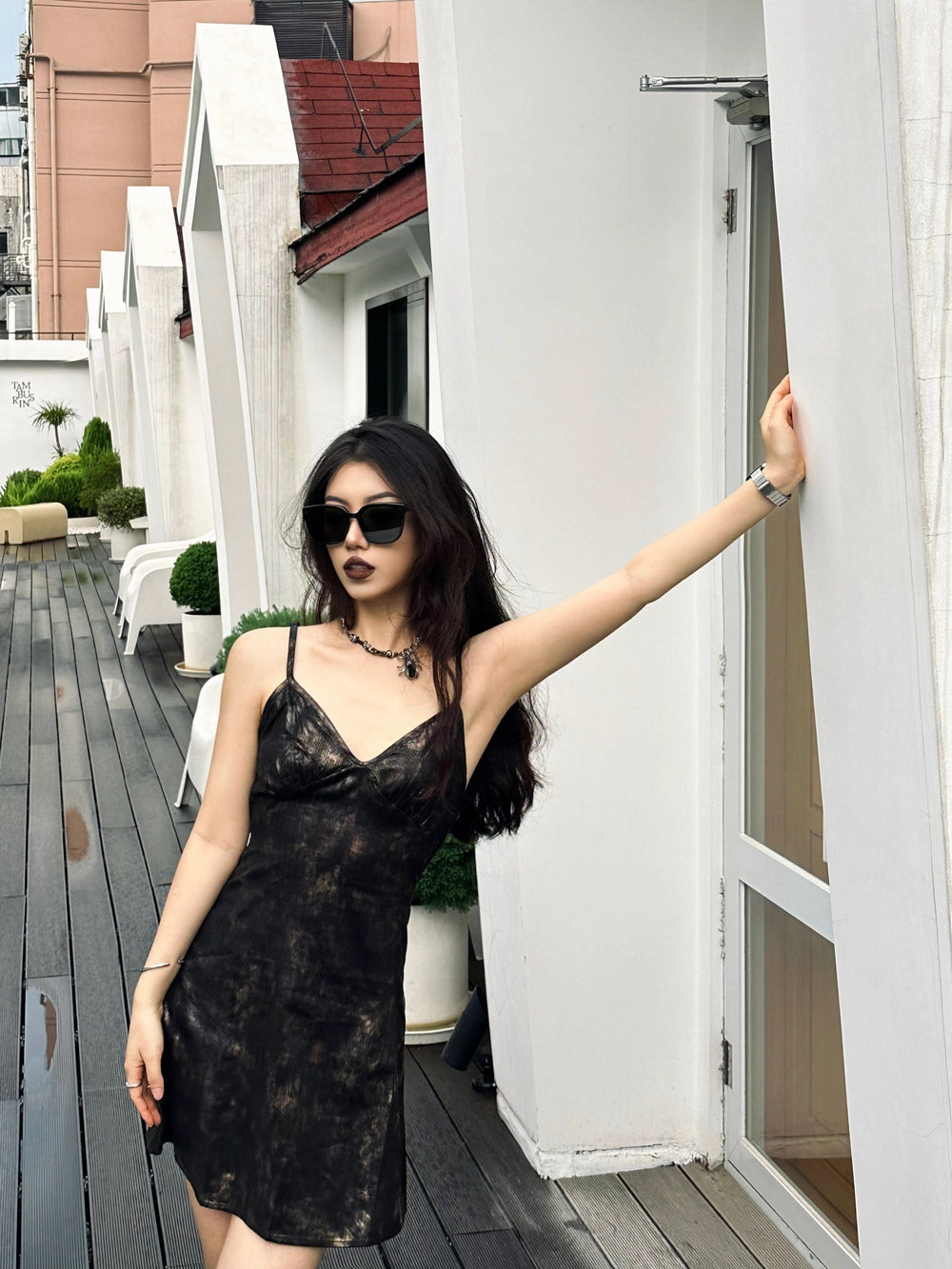 With an air of allure, a woman donning a chic black dress gracefully poses on a balcony, creating a captivating visual symphony wearing her Korean fashionable sunglasses.