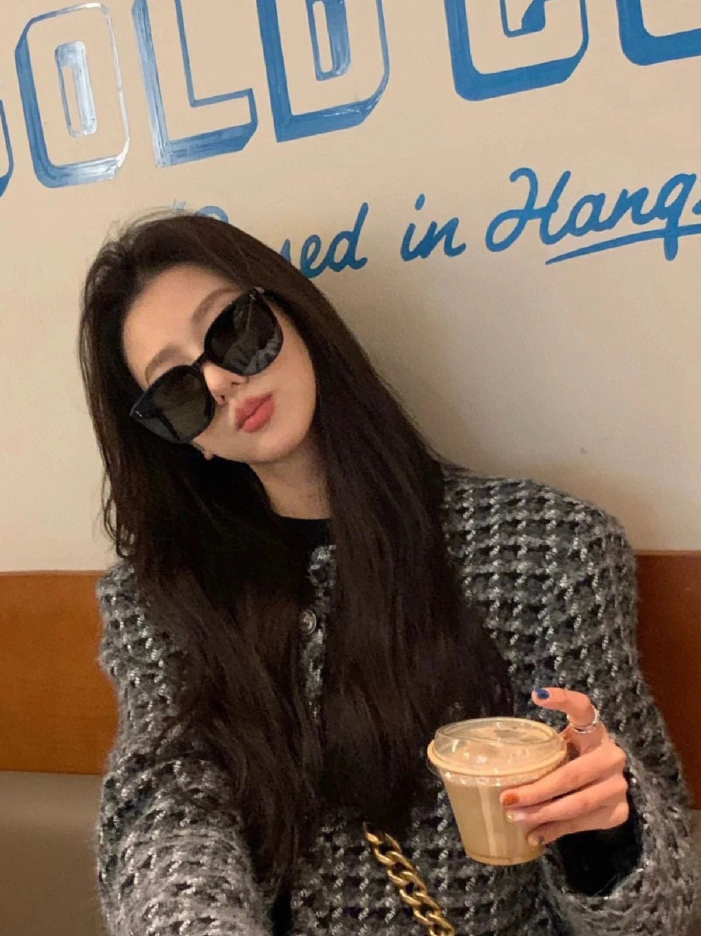 A woman with long hair and korean fashion sunglasses sitting in a booth, enjoying a moment of peace.