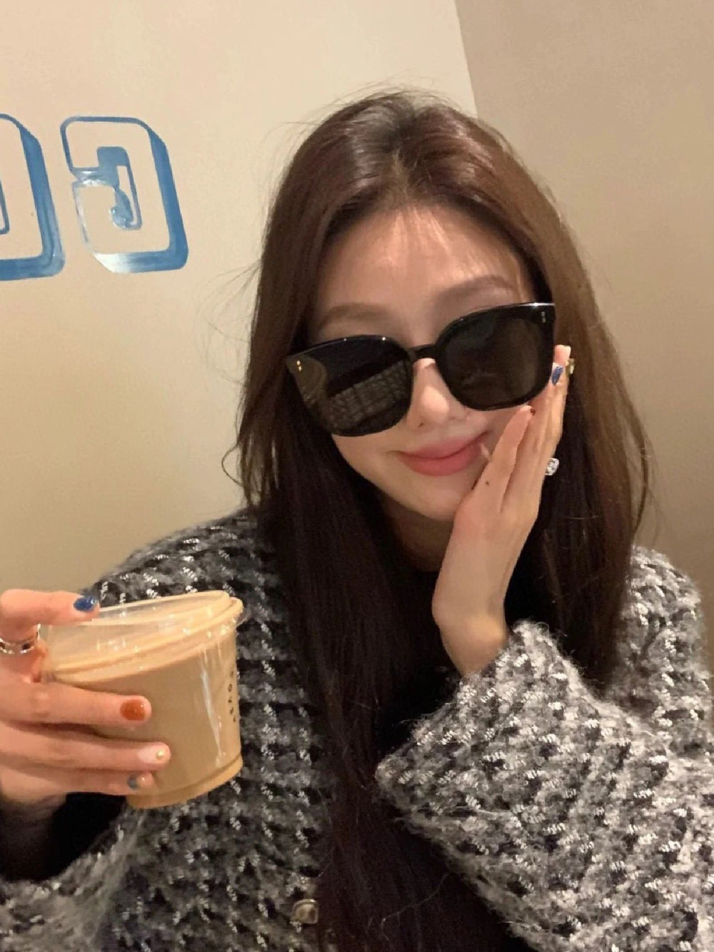 A stylish woman wearing fashionable sunglasses and holding a cup.