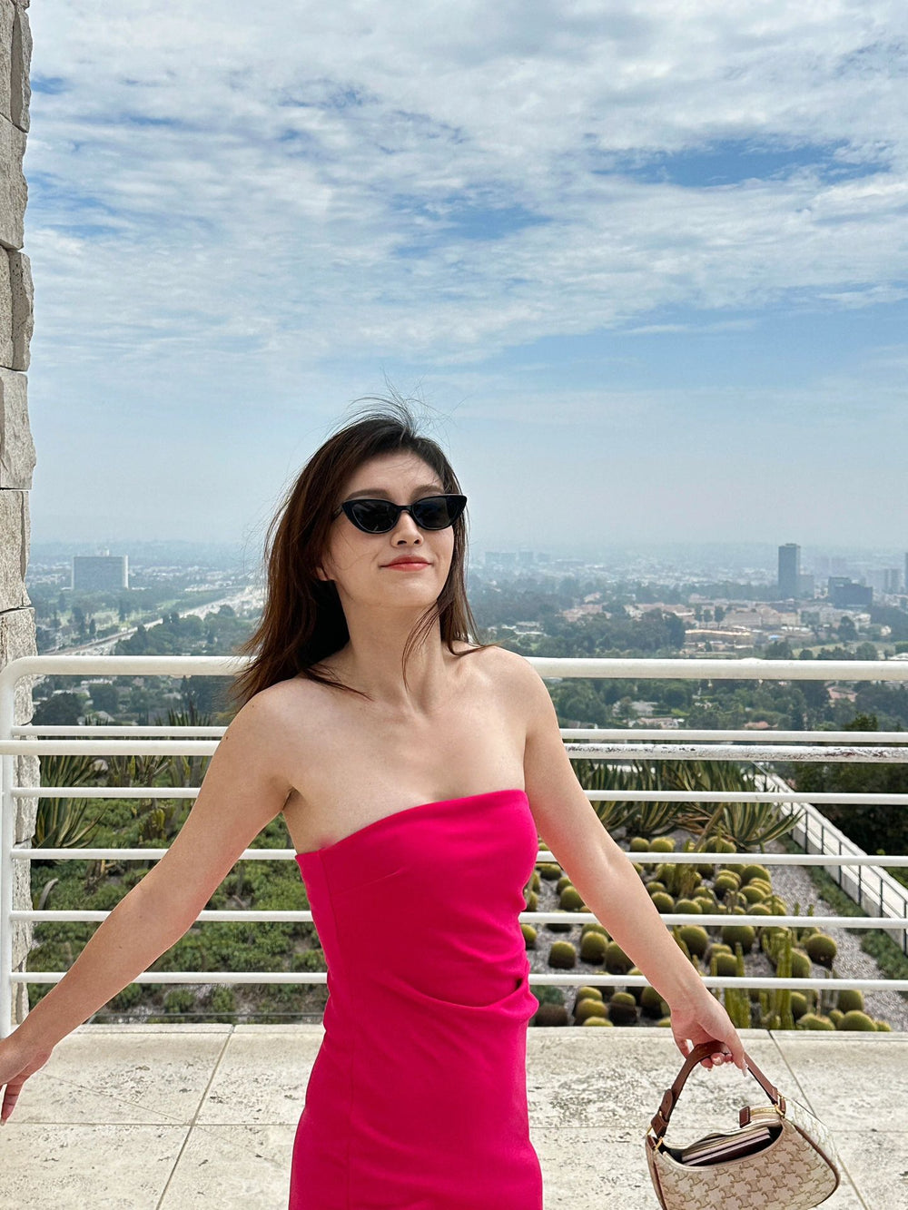 Feast your eyes on the picture of sophistication - a woman in a pink dress and sunglasses, standing on a balcony, exuding grace and charm with her Korean  fashionable sunglasses.