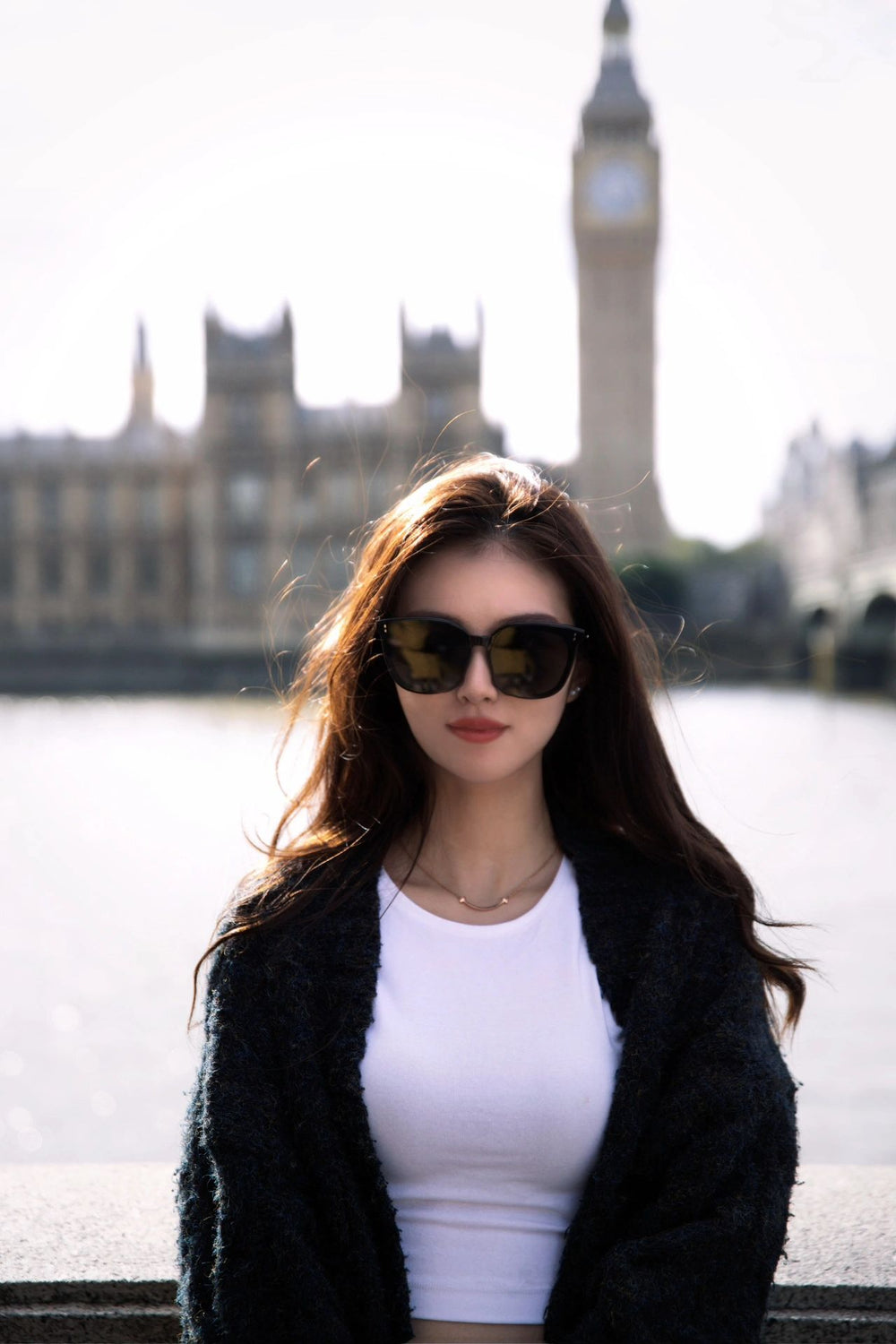 A woman in korean fashion sunglasses and white shirt stands before the iconic Big Ben.