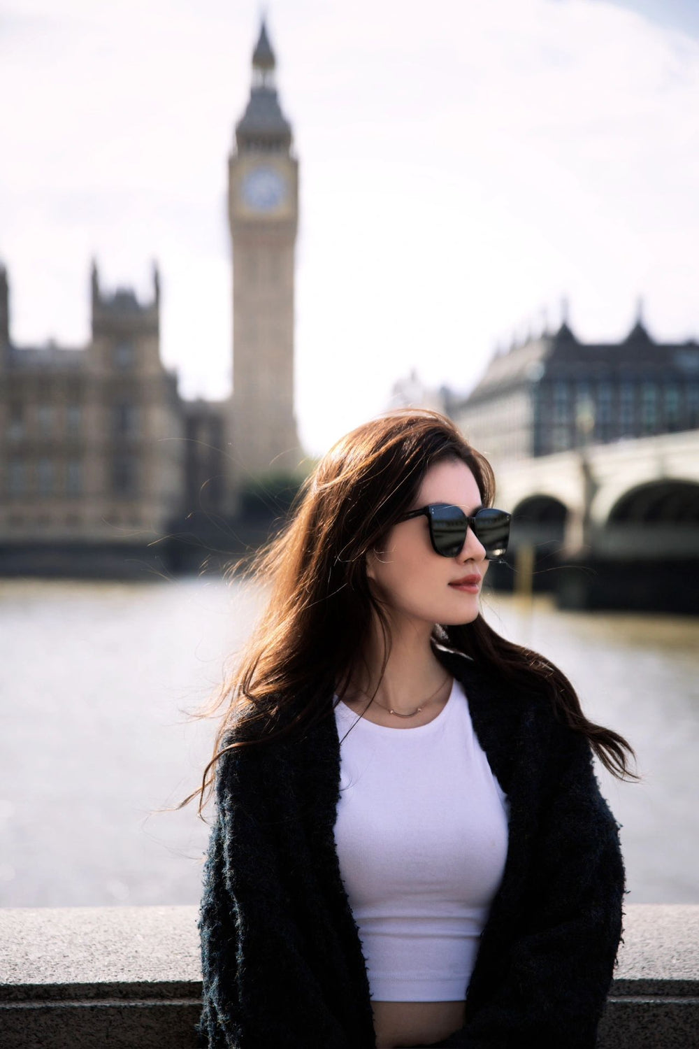 Woman in fashionable sunglasses and black jacket posing in front of Big Ben.