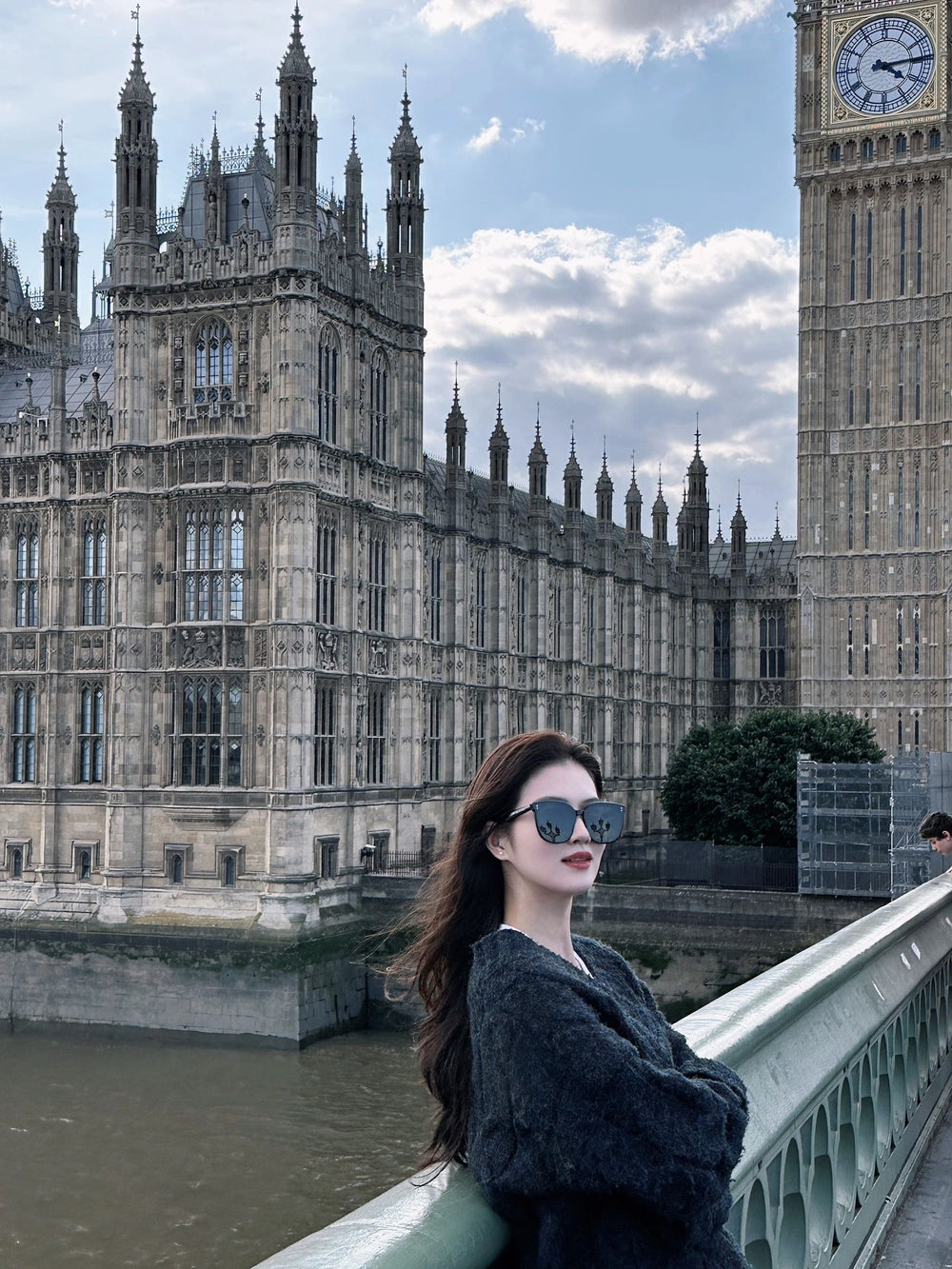  A stylish woman in designer sunglasses posing on a bridge with Big Ben in the background.