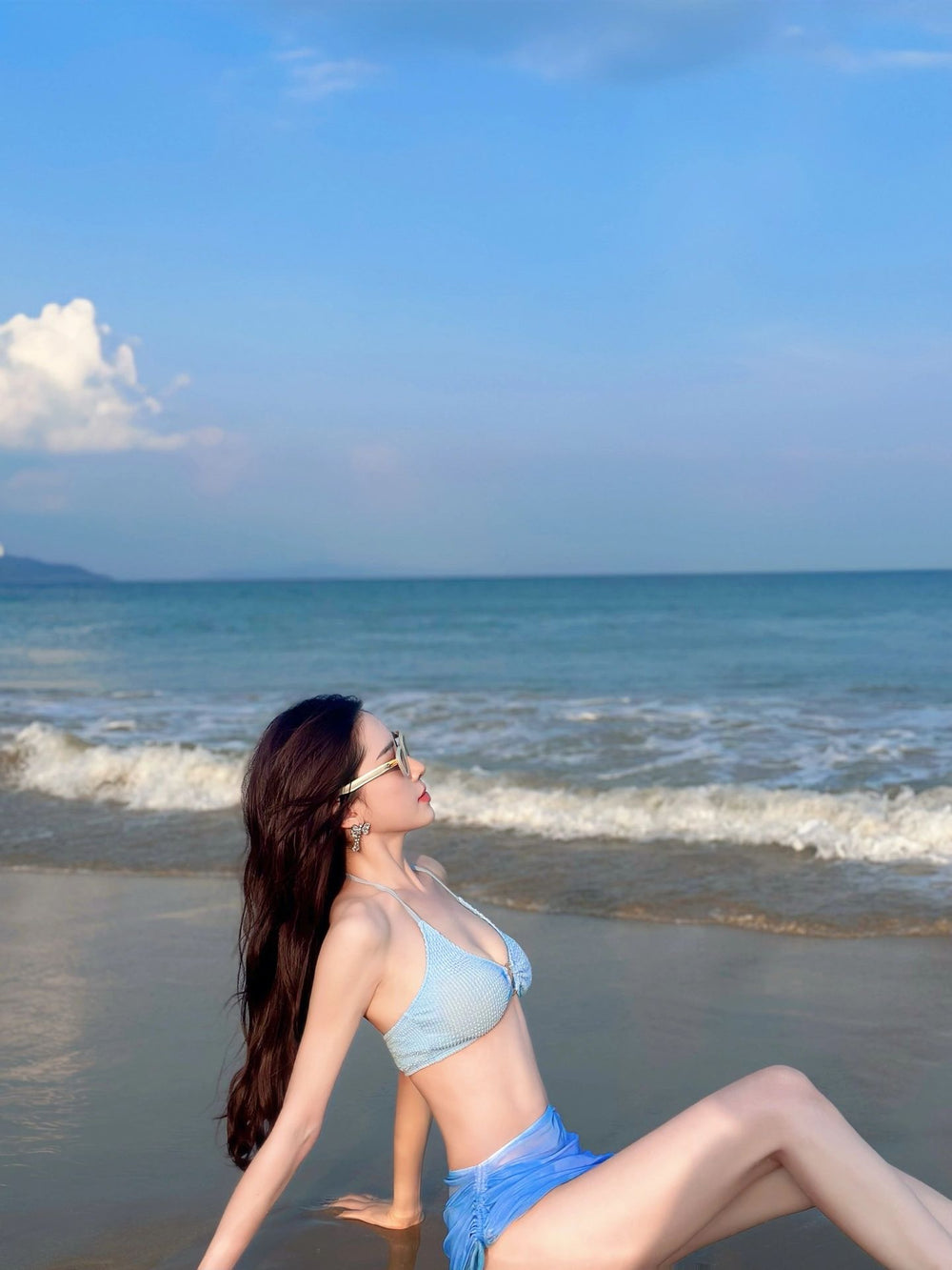 An enchanting sight of opulence and serenity: a beachside goddess adorned in a bikini, basking in the golden rays on a pristine shoreline with her Korean  fashionable sunglasses.