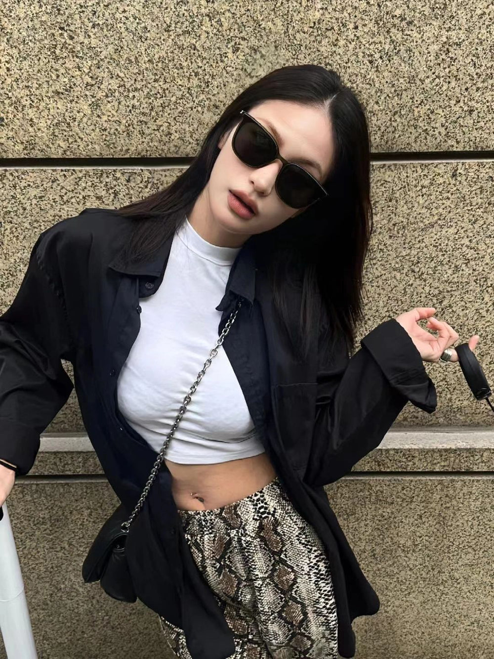 A stylish woman exudes elegance in a pristine white top and a sleek black jacket, epitomizing timeless sophistication wearing her Korean fashionable sunglasses.