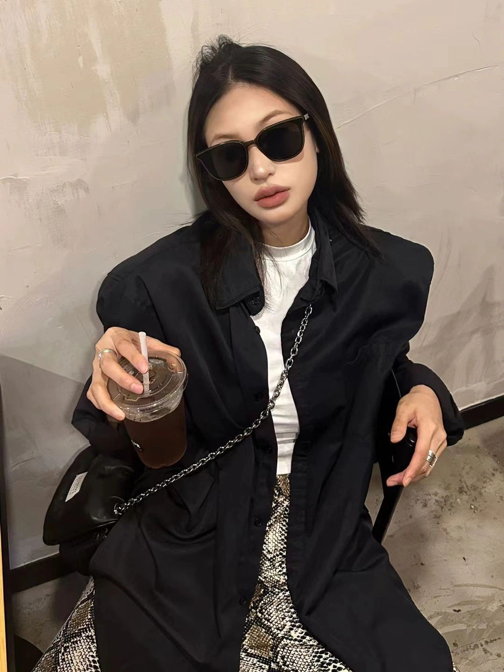 A fashionable lady wearing trendy sunglasses and a coat relaxing on a chair.