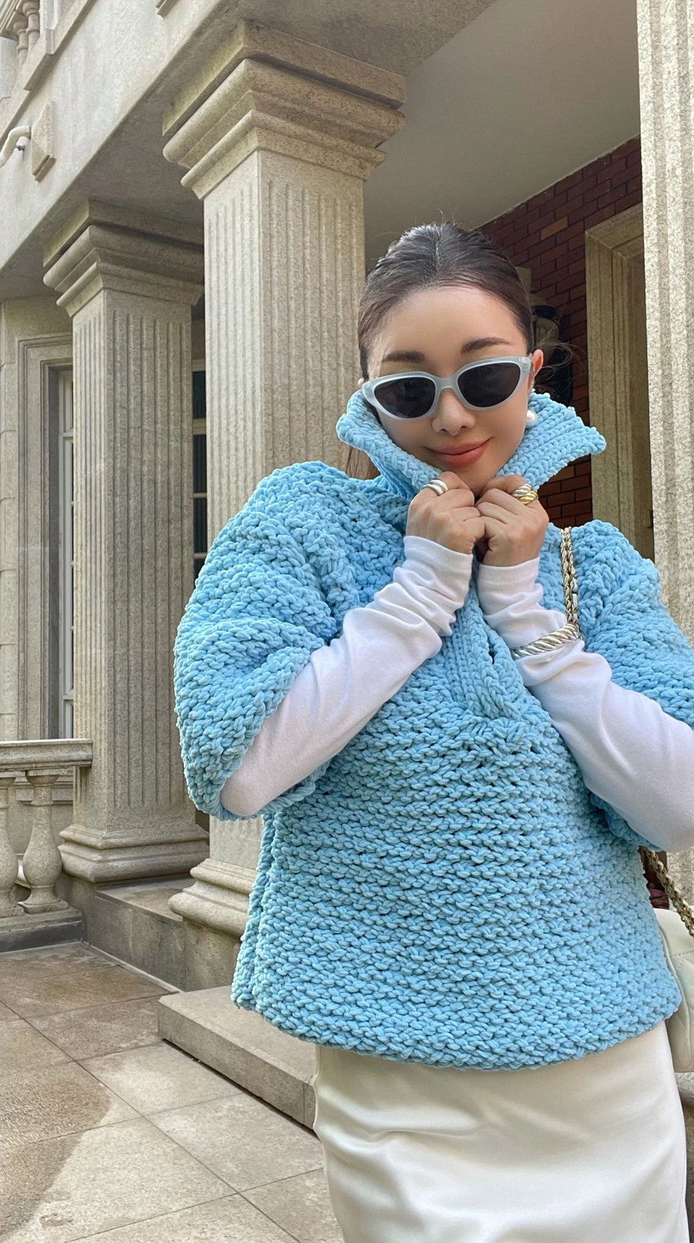 An effortlessly fashionable lady, clad in a captivating blue sweater and fashionable sunglasses, exudes an aura of refinement.