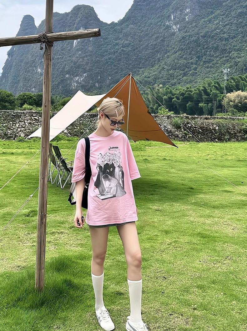 A fashionable lady, donning a pink shirt and chic sunglasses , poses gracefully next to a symbolic cross.