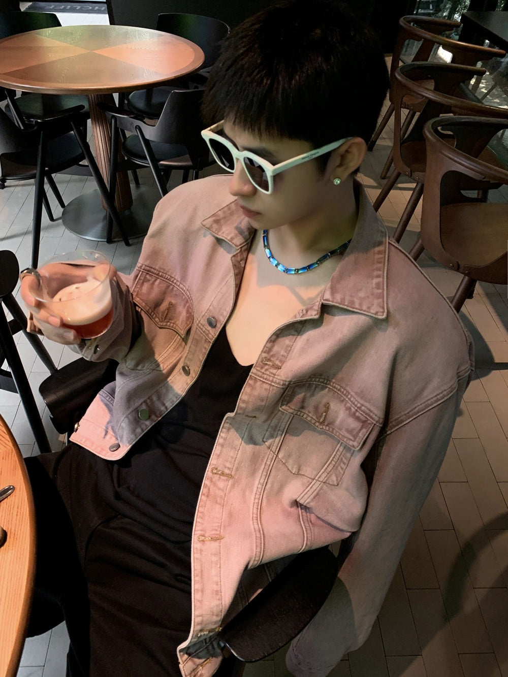 A suave gentleman, donning stylish sunglasses, enjoys a moment of leisure at a table, savoring a steaming cup of coffee.