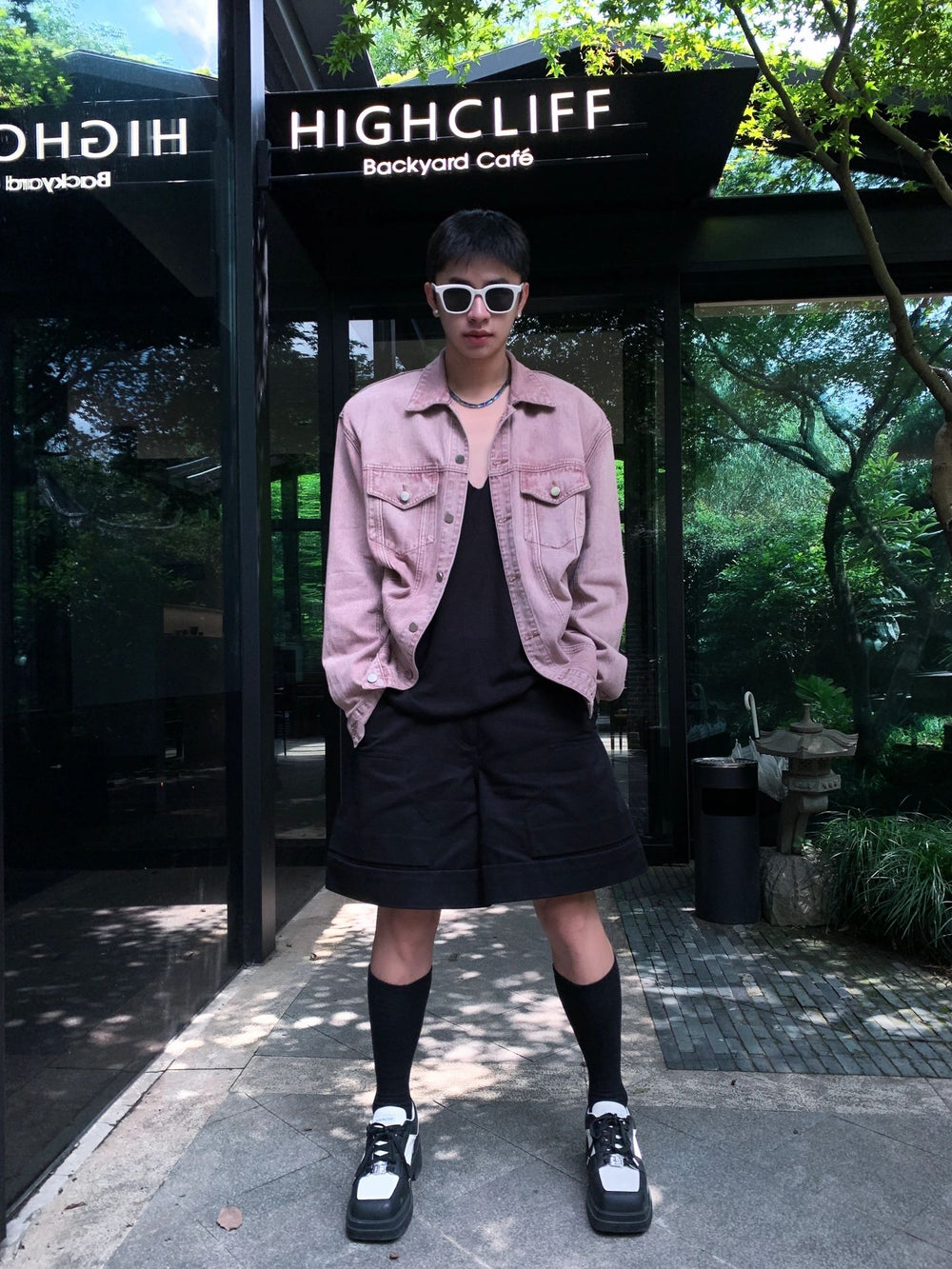 Witness the epitome of sartorial elegance as a debonair man effortlessly rocks a pink jacket and a sleek black skirt, showcasing his impeccable taste wearing his Korean fashion sunglasses.