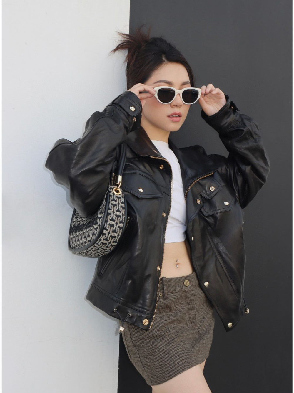 With an air of mystery, a woman exudes glamour in her black leather jacket and stylish sunglasses. Her impeccable fashion sense is captivating and alluring.