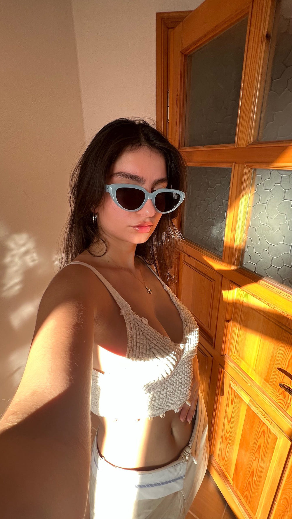 With grace and poise, a fashionable lady in a white top and stylish sunglasses immortalizes her allure through a captivating selfie.