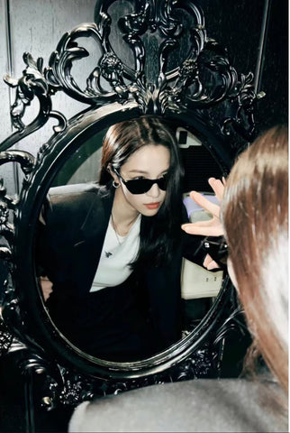 Stylish woman checking herself out in mirror while wearing sunglasses and black suit.