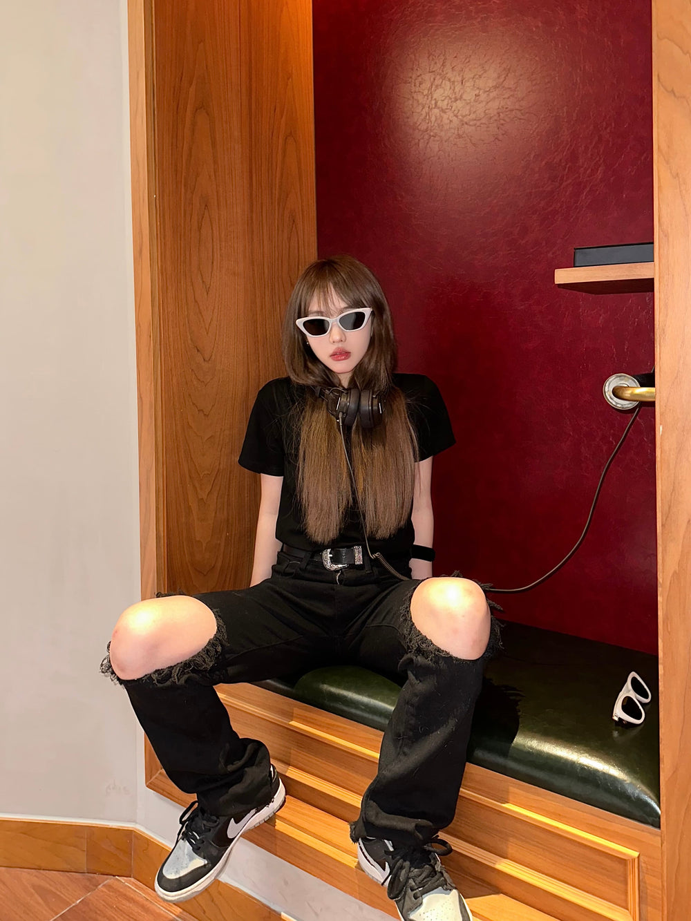 In the opulent confines of a lavishly decorated room, a person finds solace on a regal bench, exuding an air of tranquility and refinement with her trendy sunglasses.