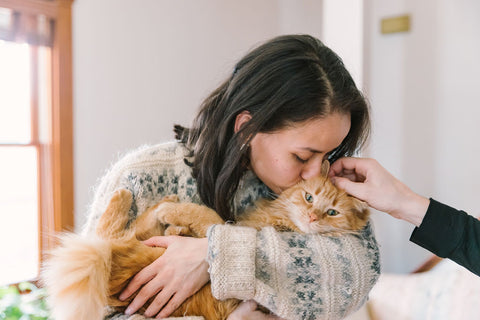 woman holds and kisses an orange cat