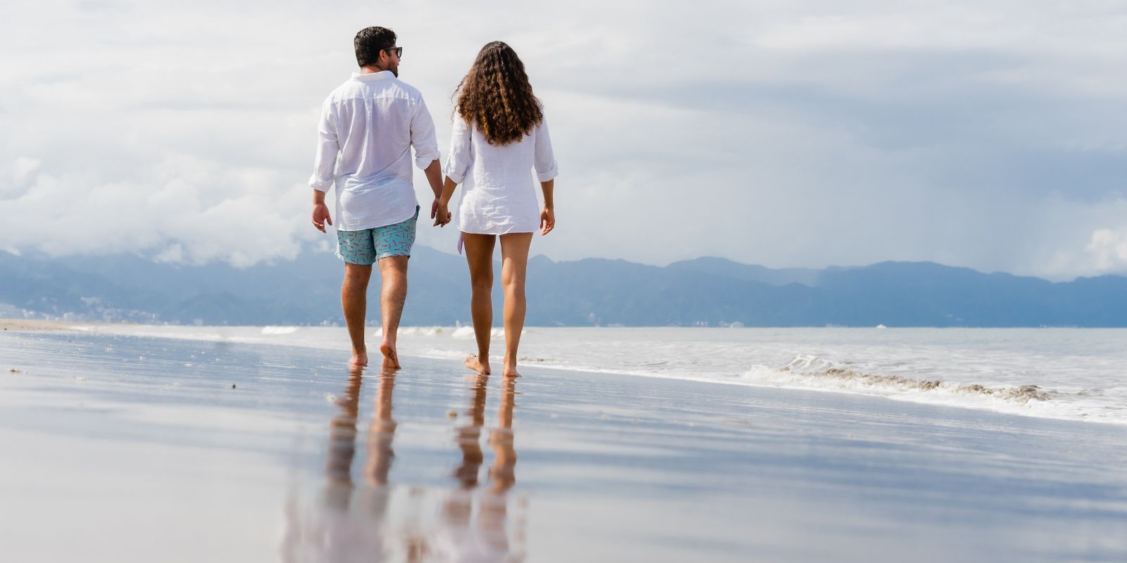 Un couple se tenant par la main et marchant sur la plage.