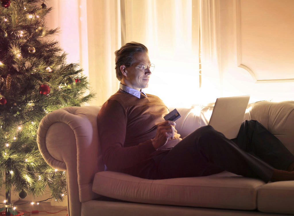 Old White Man Sitting On Couch in Front of Christmas Tree Ordering a Pump On His Laptop with Credit Card Confidentially