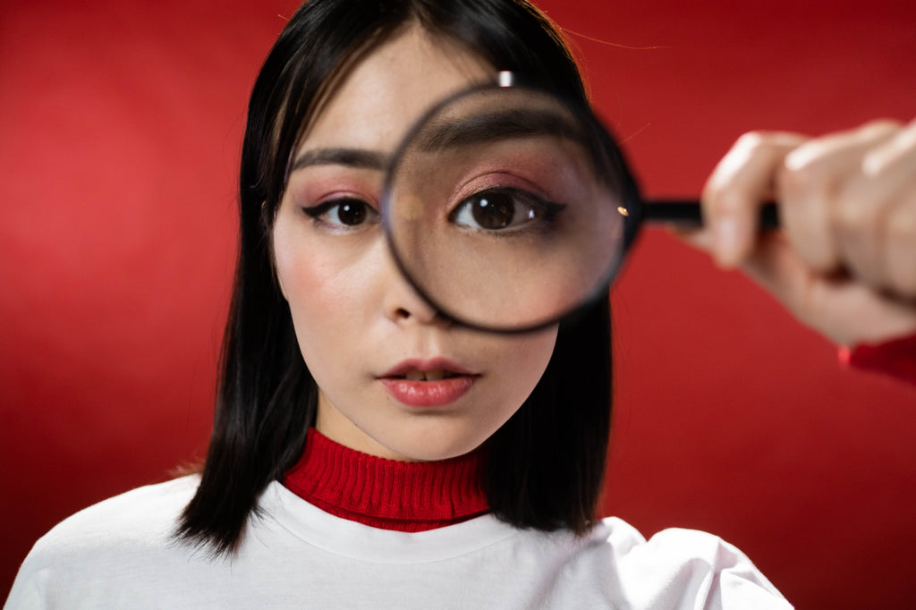 Asian Woman Looking Through Magnifying Glass at Penis Pump Man