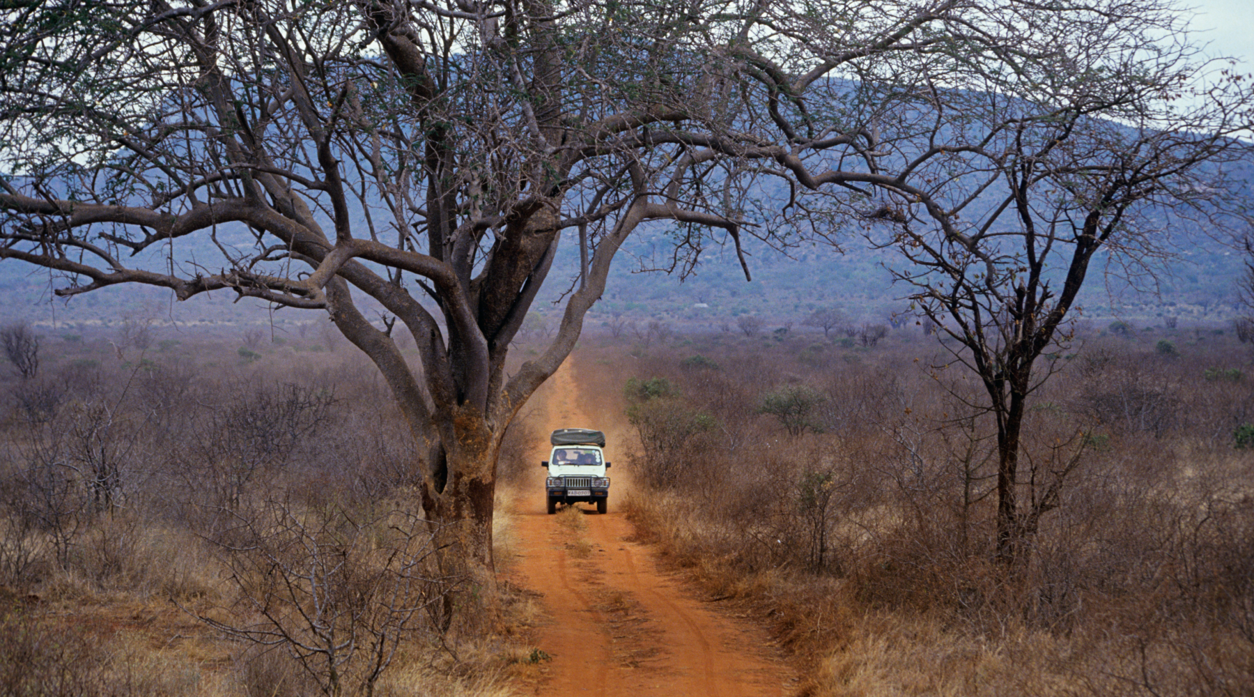 Small, white, overlanding vehicle travels along a dirt road in Africa.
