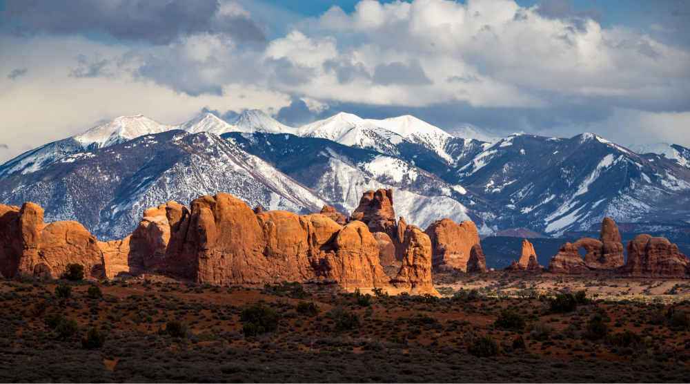 Scenic red and orange Moab Desert in the foreground with Snow-Capped La Sal Mountains behind.