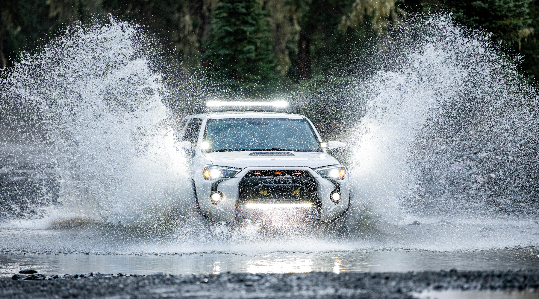 White Toyota 4 Runner crosses a river with black rock beach.