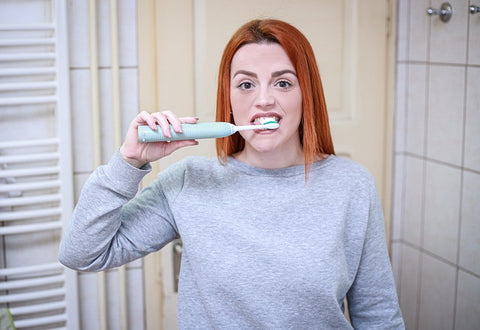 A woman brushing her teeth with an electric toothbrush