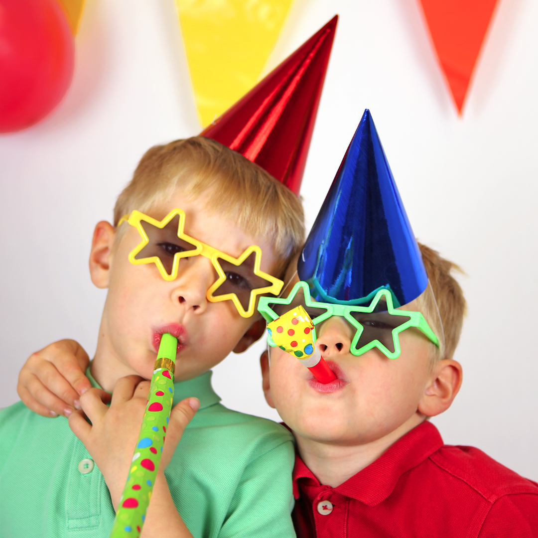 Two boys wearing party hats and blowing whistles.