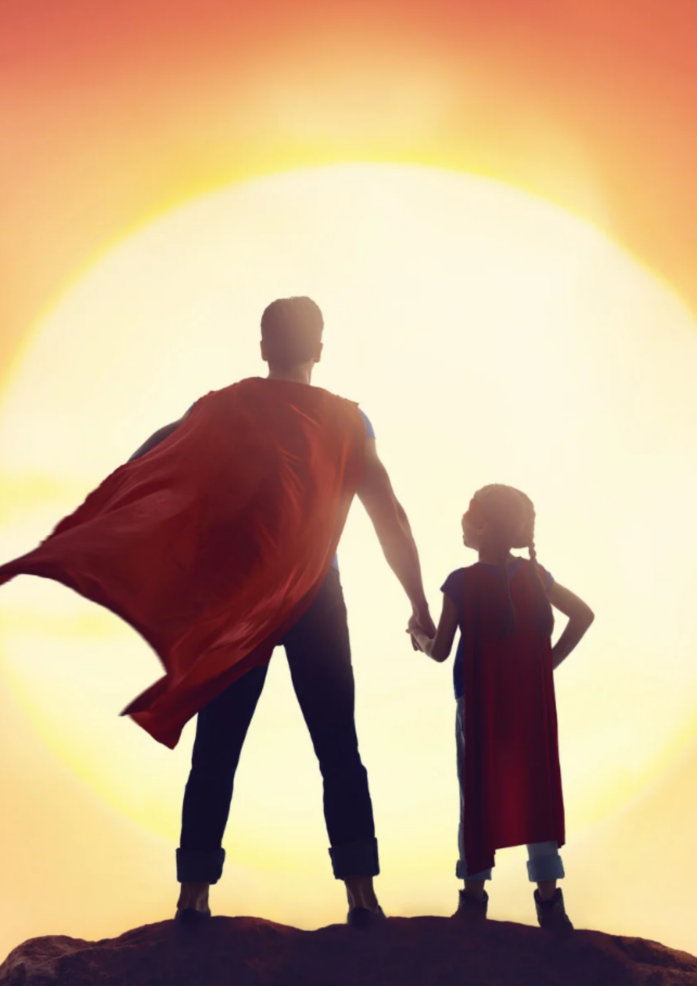 Father in Superman costume standing with his daughter in front of the sun.