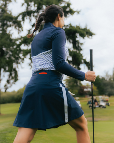 A woman in a blue skirt and a blue long sleeved shirt, holding a golf club