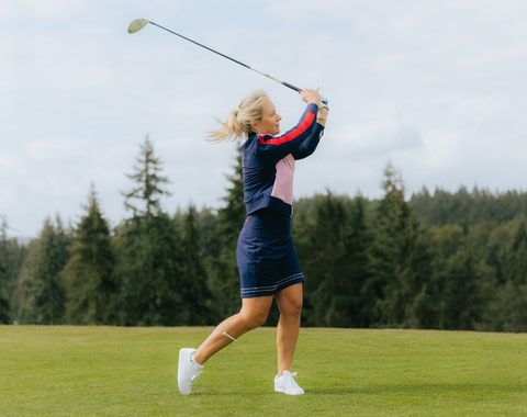 A woman wearing a matching blue jacket and skirt, swinging a golf club