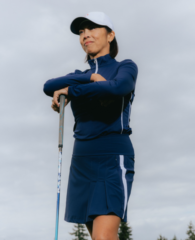 A woman wearing a dark blue outfit, standing with a golf club