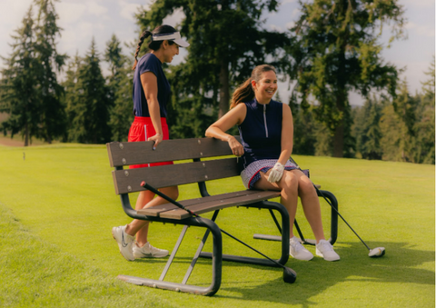 A woman in a dark blue shirt and red skirt standing y a woman in a dark blue dress