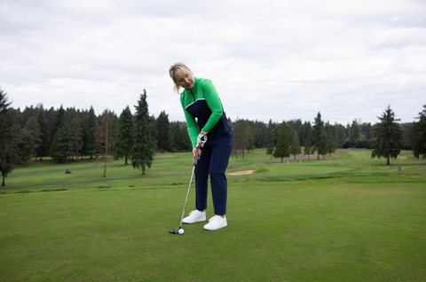 A woman wearing pants and a long-sleeved shirt, holding a golf club