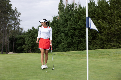 A woman wearing a skirt, and matching shirt on the golf course