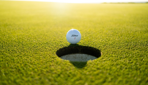 A white golf ball next to a hole on the golf course