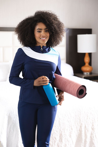 A woman wearing a dark blue outfit, holding a yoga mat