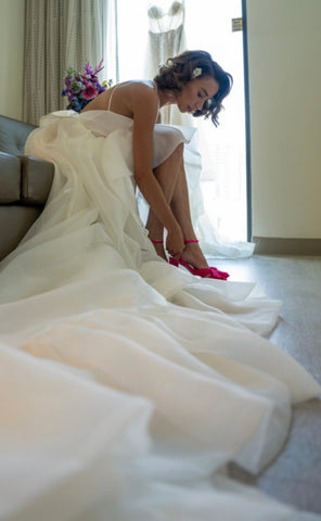 A custom made ruffled organza wedding gown by Margo West on a pretty woman putting on her shoes.