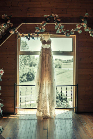 Lace wedding gown hanging in the doorway with sunshine