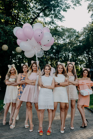 A bride with her bridesmaids lined up holding balloons smiling.