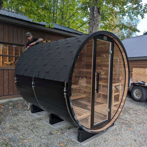 Black cedar barrel sauna with glass door in yard 