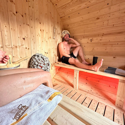 man smiling inside barrel sauna with huum heater and red led lights in sauna