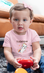 Awareness Infant Clothes. Baby girl holding a red toy wearing an awareness t-shirt with a flying unicorn that reads, YOUnique.