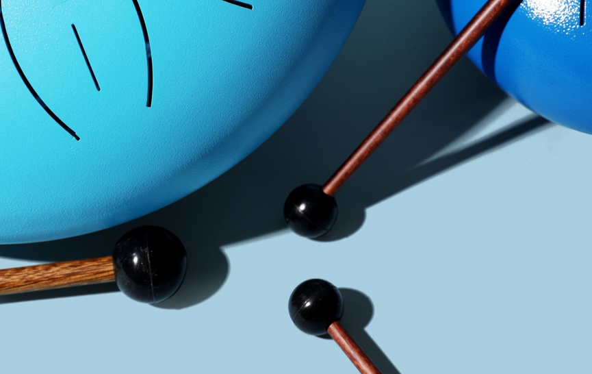 Close-up of mallets resting on blue kettle drums with shadows.