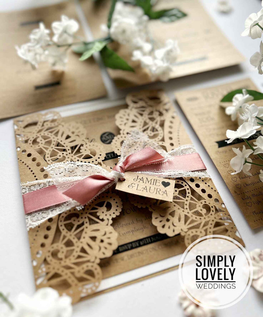 Handmade wedding invitation in laser cut pocket.  Kraft laser cut invitation with a dusky pink bow and lace detail.  Perfect for a rustic or garden wedding theme.