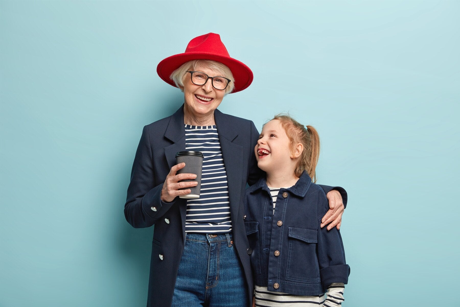 portrait-happy-fashionable-granny-small-cute-child-spend-spare-time-together-drinks-takeaway-coffee-cuddle-have-friendly-relationships-wear-denim-clothes-stand-blue-wall_273609-26791