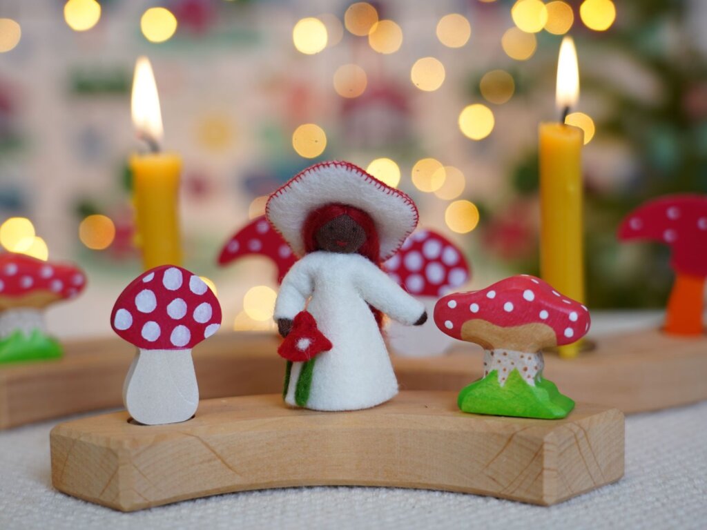 A celebration ring with wooden Fly agaric mushroom decorations, candles and an ambrosius felt toadstool fairy in the centre. 