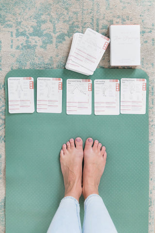 Yogi standing on her mat with her yoga cards laid out in front of her