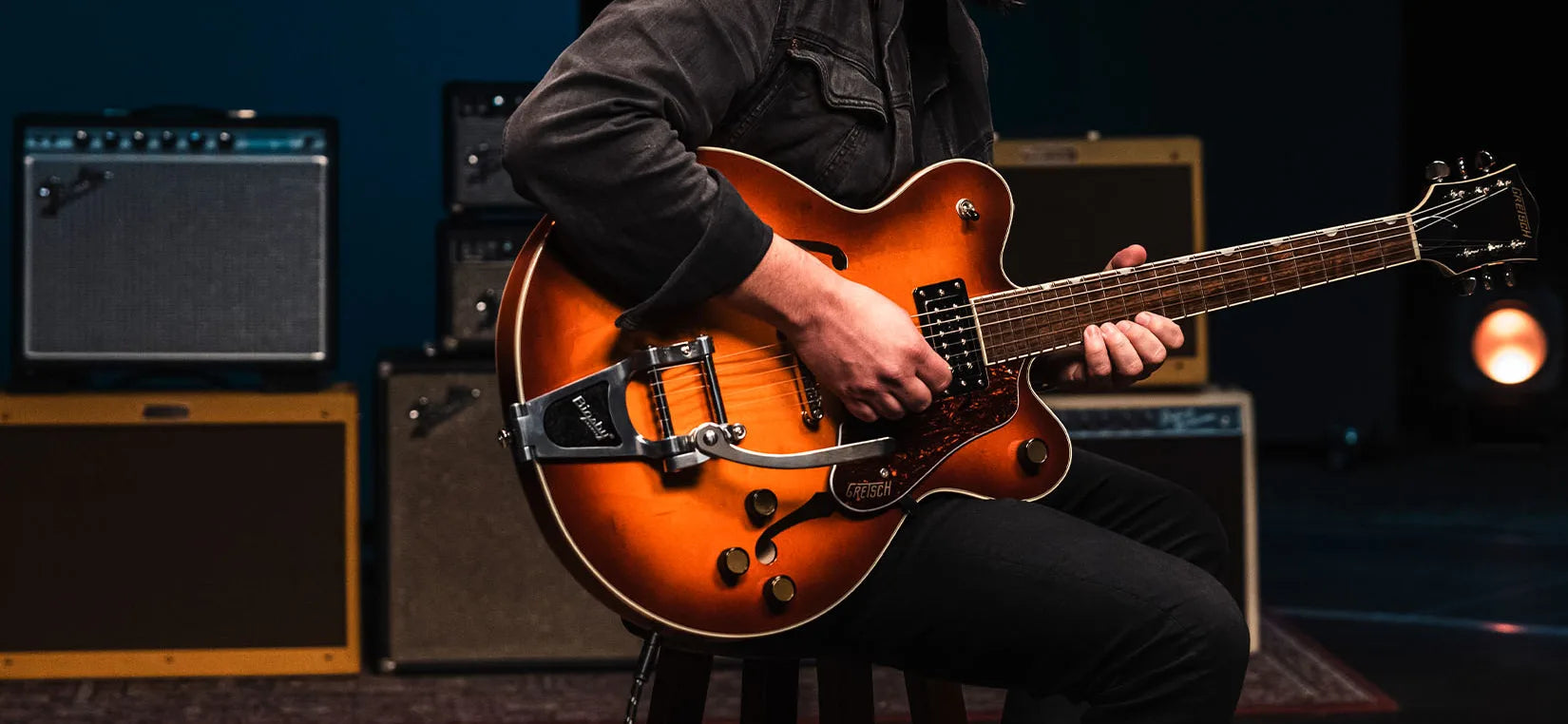 Guitarrista sentado tocando guitarra gretsch en el fondo amplificadores para guitarra